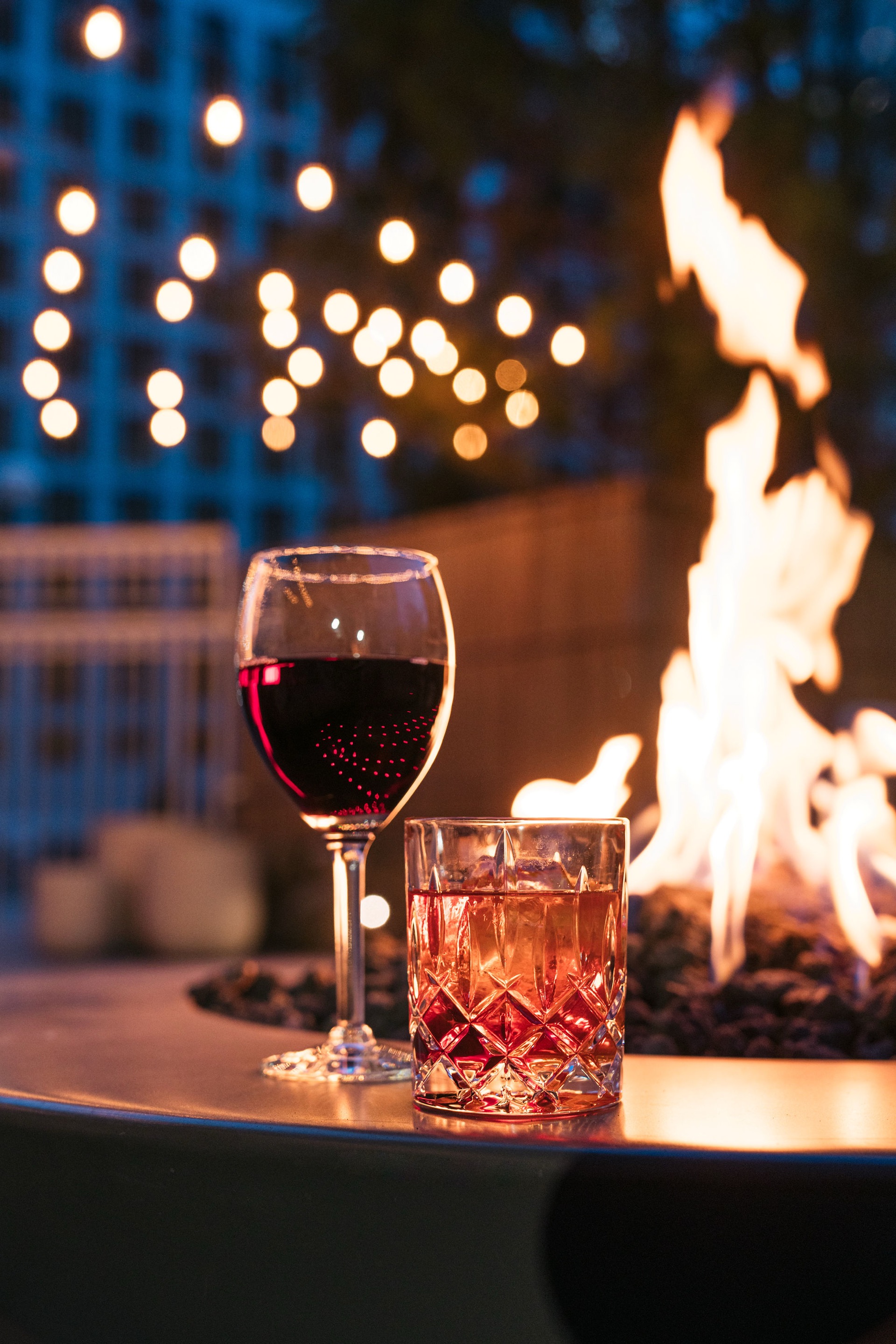 Wine and cocktail by the firepit at twilight with bokeh lights